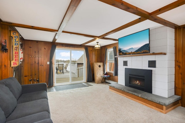 living area with a tiled fireplace, wood walls, coffered ceiling, and carpet