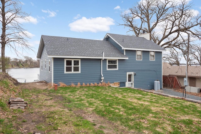 back of house featuring a yard, a shingled roof, a chimney, and a water view