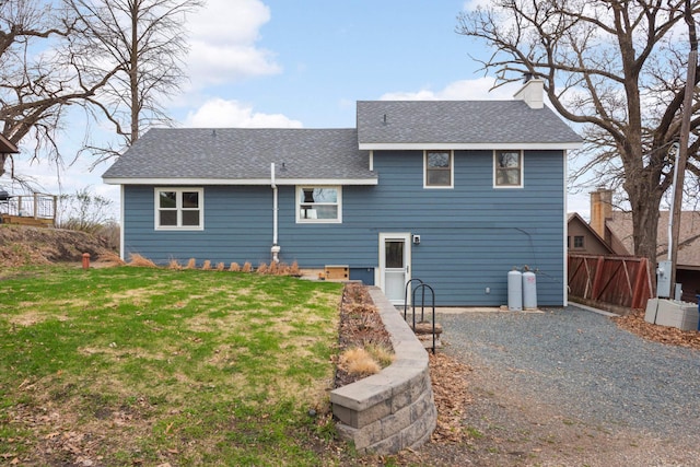 rear view of property with a yard, roof with shingles, a chimney, and fence