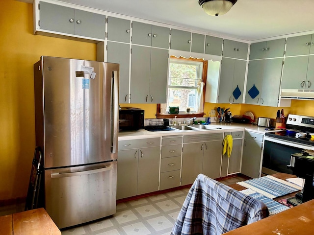kitchen featuring light floors, light countertops, under cabinet range hood, a sink, and stainless steel appliances