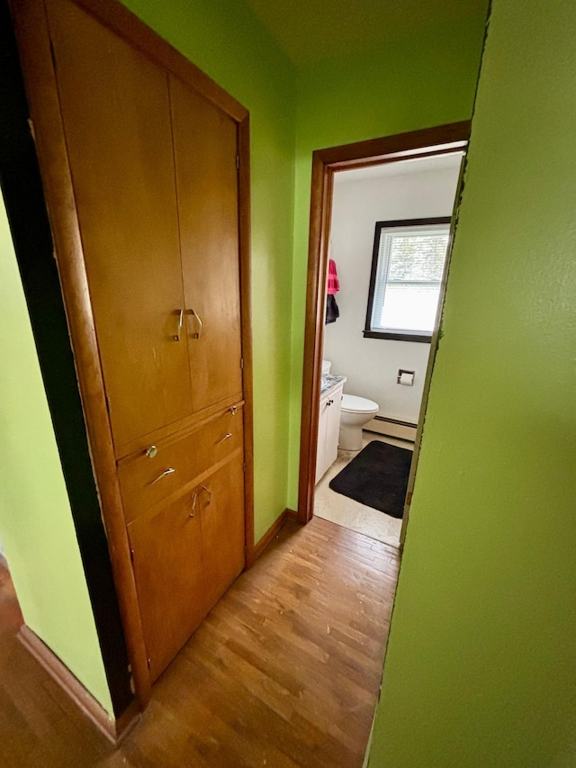 hall featuring baseboards, a baseboard heating unit, and light wood-style flooring