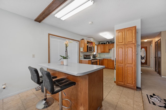 1601 5th Ave, Grand Rapids, MN 55744 - kitchen featuring brown cabinetry, stainless steel appliances, light countertops, a kitchen bar, and baseboards