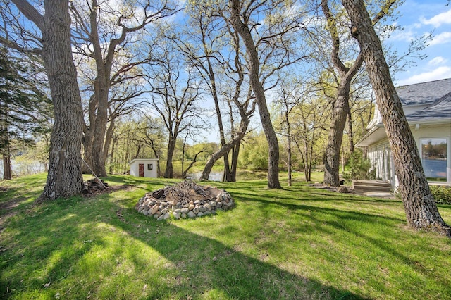 view of green lawn featuring a shed, an outdoor structure, and a fire pit