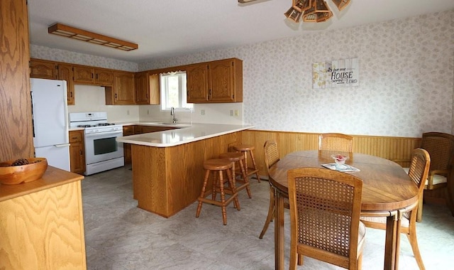 44172 Mosquito Heights Rd, Perham, MN 56573 - kitchen with white appliances, a peninsula, a wainscoted wall, a sink, and brown cabinets