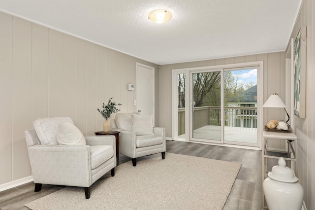 living area with baseboards, a textured ceiling, and wood finished floors
