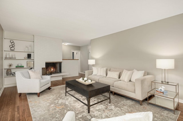 living room with baseboards, a brick fireplace, and wood finished floors
