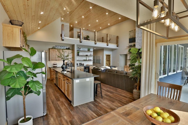 kitchen with a sink, high vaulted ceiling, appliances with stainless steel finishes, a kitchen bar, and dark countertops