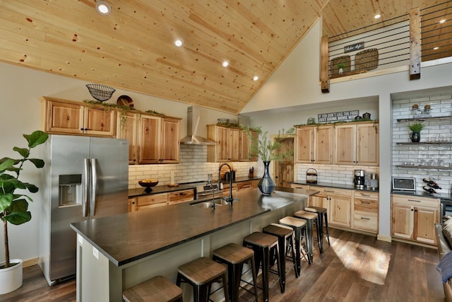 kitchen with stainless steel refrigerator with ice dispenser, wall chimney range hood, dark countertops, wood ceiling, and a sink