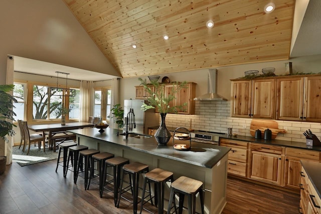 kitchen with wall chimney range hood, dark countertops, a breakfast bar, dark wood-style floors, and decorative backsplash