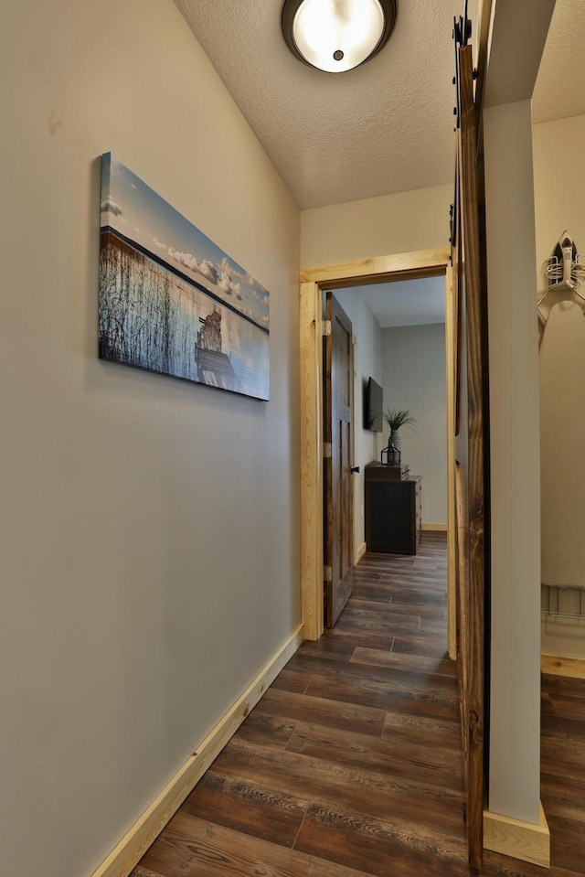 hall with dark wood-type flooring, a textured ceiling, and baseboards