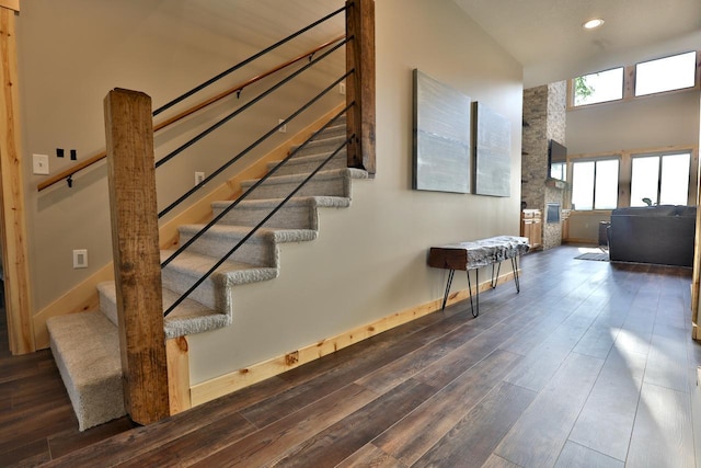 stairway featuring hardwood / wood-style floors, recessed lighting, baseboards, a high ceiling, and a stone fireplace
