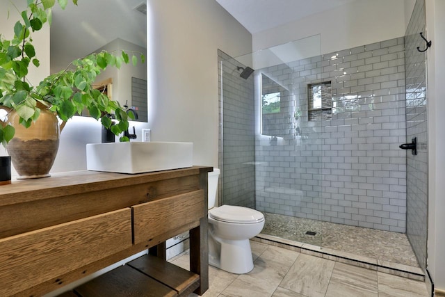 full bathroom featuring tiled shower, toilet, and vanity