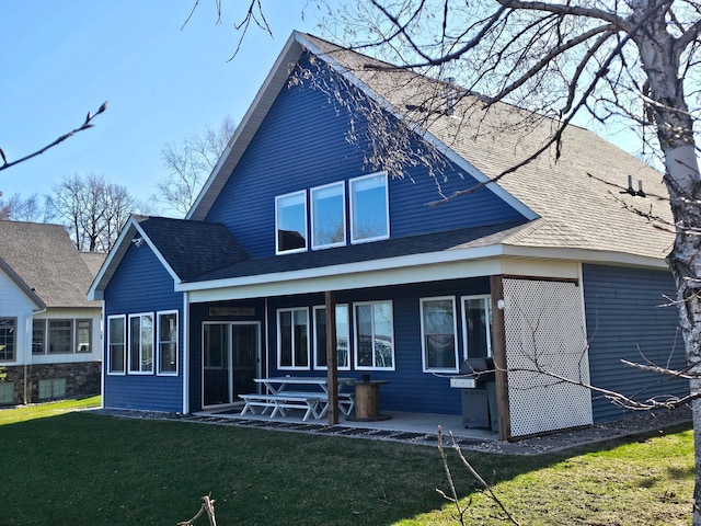 rear view of property featuring a patio area, a yard, and a shingled roof