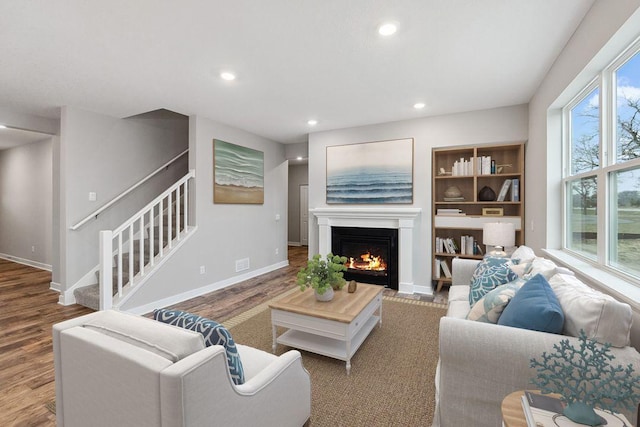 living room with recessed lighting, stairway, a warm lit fireplace, wood finished floors, and baseboards