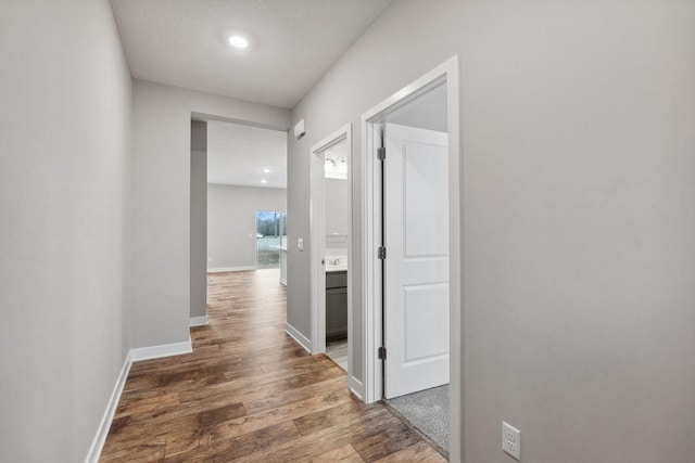 hallway featuring baseboards, wood finished floors, and recessed lighting