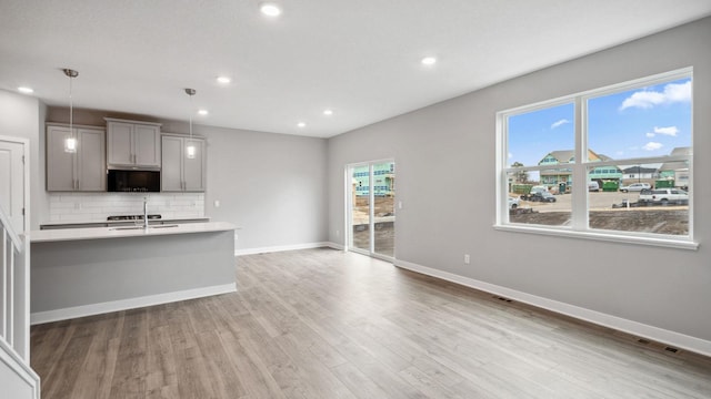 kitchen with a sink, light countertops, gray cabinets, light wood-style flooring, and backsplash