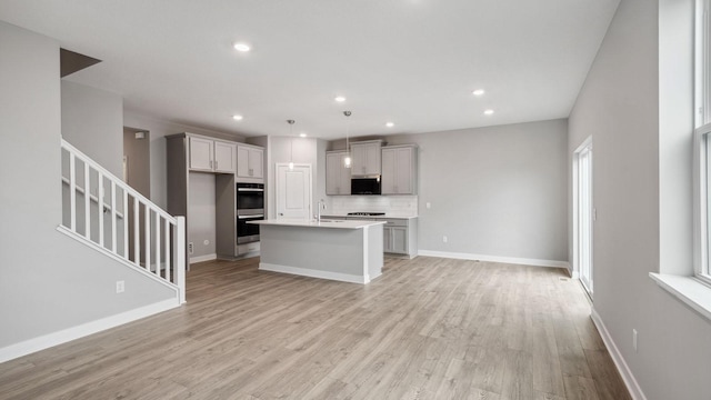 kitchen featuring recessed lighting, light wood finished floors, a kitchen island with sink, tasteful backsplash, and open floor plan