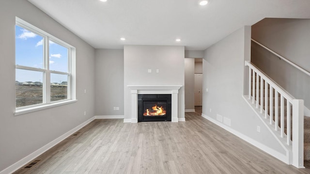 unfurnished living room with recessed lighting, a glass covered fireplace, wood finished floors, and stairs