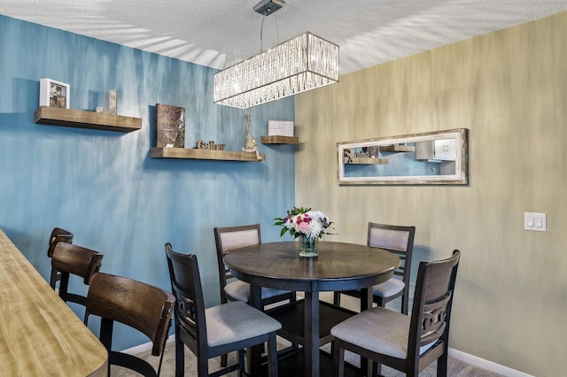 carpeted dining area with a textured ceiling, a notable chandelier, and baseboards