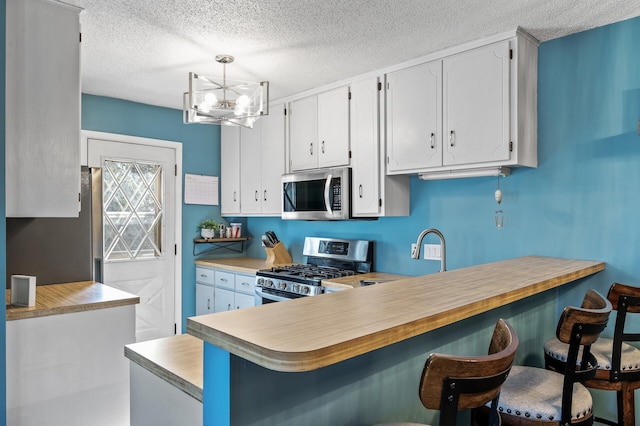 kitchen with light countertops, a textured ceiling, a chandelier, stainless steel appliances, and white cabinetry
