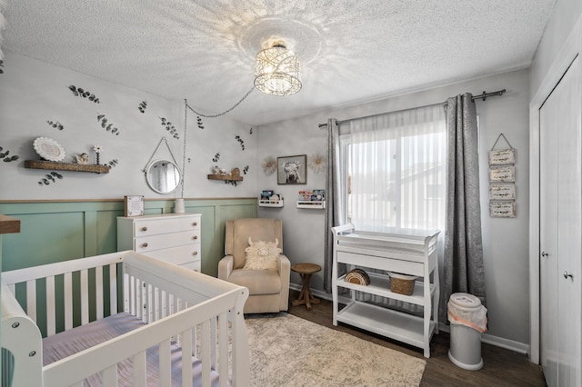 bedroom with a closet, wainscoting, wood finished floors, a textured ceiling, and a crib