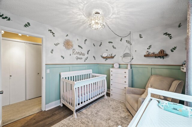 bedroom featuring a nursery area, a notable chandelier, a textured ceiling, and wood finished floors