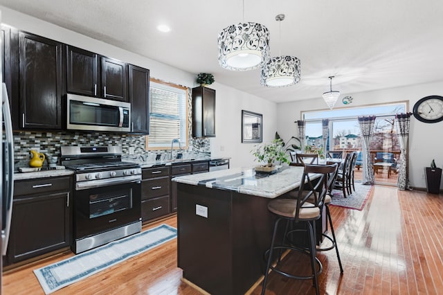 kitchen featuring stainless steel appliances, light wood-style flooring, a kitchen breakfast bar, tasteful backsplash, and a kitchen island