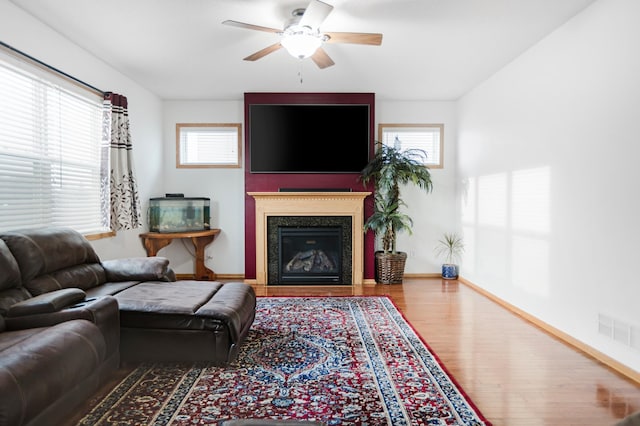 living room with wood finished floors, a glass covered fireplace, ceiling fan, baseboards, and visible vents