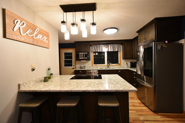 1164 Hawthorn St, Red Wing, MN 55066 - kitchen featuring appliances with stainless steel finishes, a peninsula, dark brown cabinets, a kitchen breakfast bar, and a textured ceiling