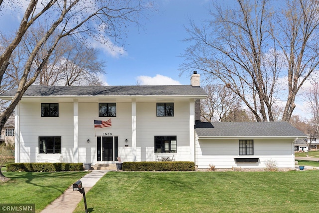 neoclassical / greek revival house with roof with shingles, a chimney, and a front lawn