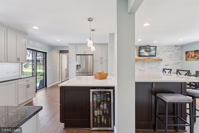 kitchen featuring stainless steel fridge with ice dispenser, beverage cooler, a kitchen breakfast bar, wood finished floors, and backsplash