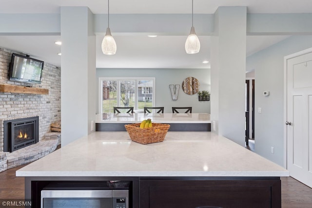 kitchen featuring pendant lighting, stainless steel microwave, dark wood-style floors, and a fireplace