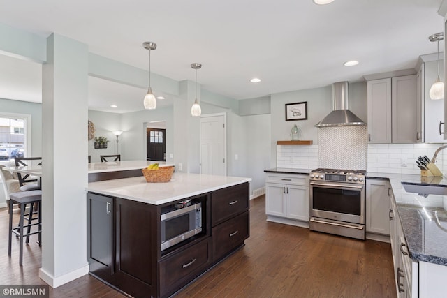 kitchen with dark wood-style flooring, tasteful backsplash, a sink, stainless steel appliances, and wall chimney exhaust hood