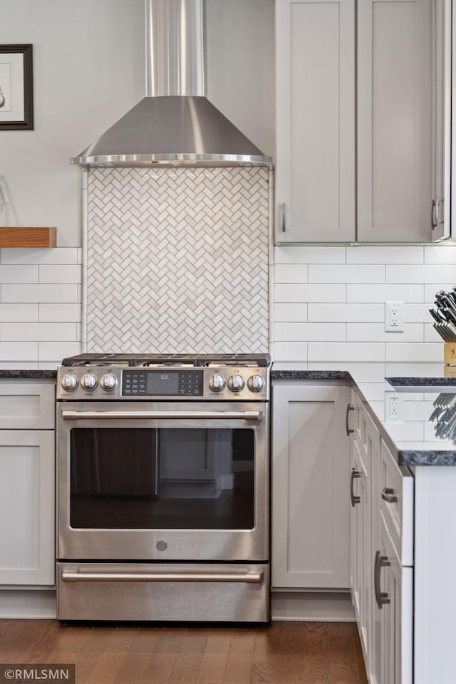 kitchen with wood finished floors, stainless steel gas range oven, wall chimney range hood, and tasteful backsplash