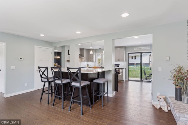 kitchen with a breakfast bar area, light countertops, dark wood-style floors, recessed lighting, and wall chimney exhaust hood