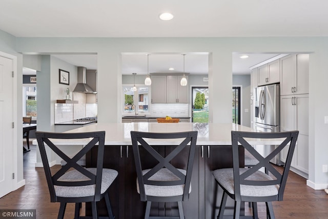 kitchen with stainless steel refrigerator with ice dispenser, a sink, wall chimney range hood, and light countertops