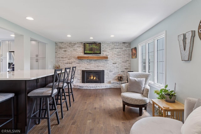 living area with recessed lighting, a brick fireplace, and dark wood finished floors