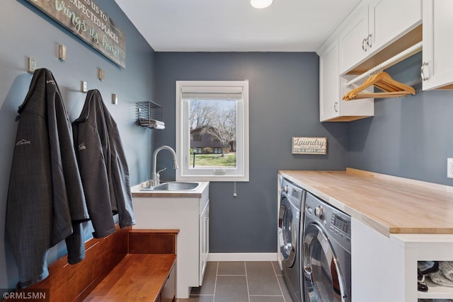laundry area with dark tile patterned floors, cabinet space, a sink, baseboards, and washer and dryer