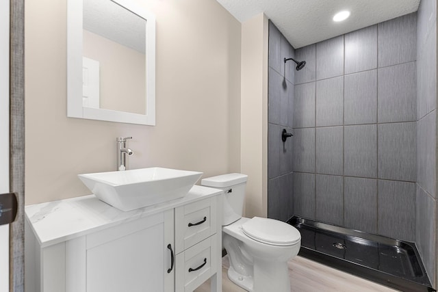 1101 8th Ave SW, Isanti, MN 55040 - bathroom with a textured ceiling, toilet, tiled shower, vanity, and wood finished floors
