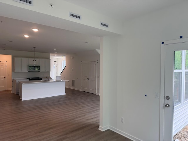 kitchen featuring stainless steel microwave, dark wood-style flooring, baseboards, a sink, and a center island with sink