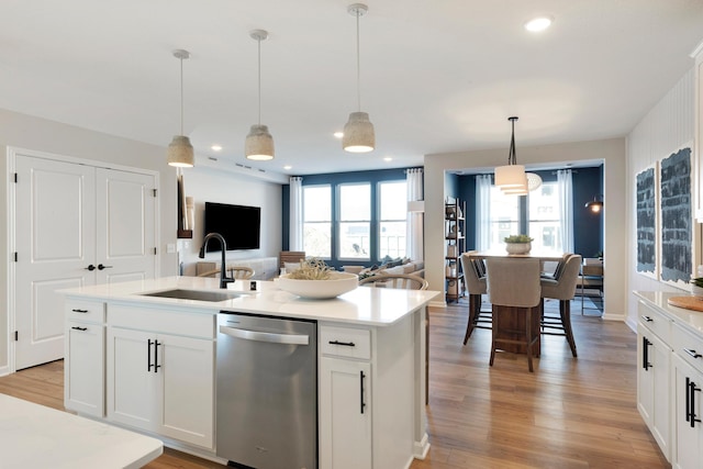 kitchen featuring stainless steel dishwasher, a sink, light wood-style floors, light countertops, and open floor plan