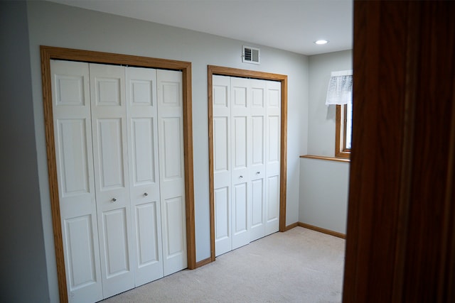 unfurnished bedroom with light colored carpet, visible vents, baseboards, recessed lighting, and multiple closets