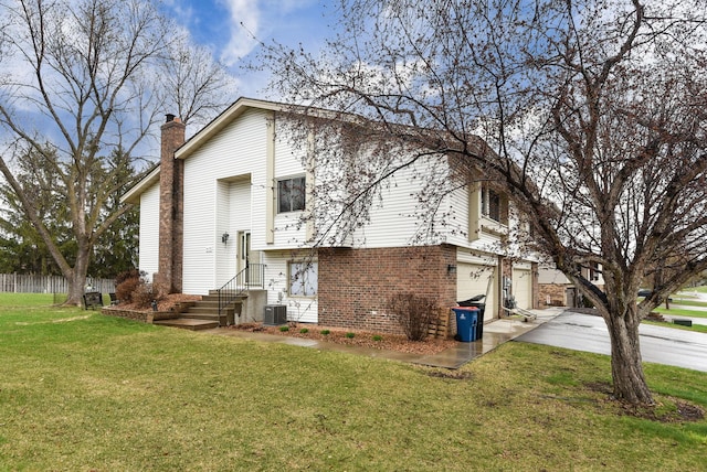 rear view of house with brick siding, a garage, a chimney, concrete driveway, and a lawn