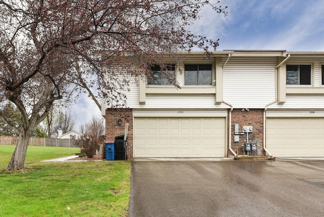 view of side of home with fence, an attached garage, brick siding, a yard, and driveway