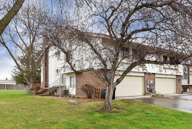 view of side of home with fence, aphalt driveway, brick siding, central air condition unit, and a yard