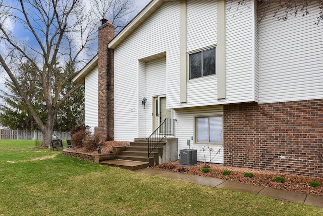 rear view of property with fence, a chimney, brick siding, central air condition unit, and a yard