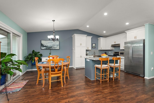 kitchen featuring decorative backsplash, a kitchen island, under cabinet range hood, appliances with stainless steel finishes, and vaulted ceiling