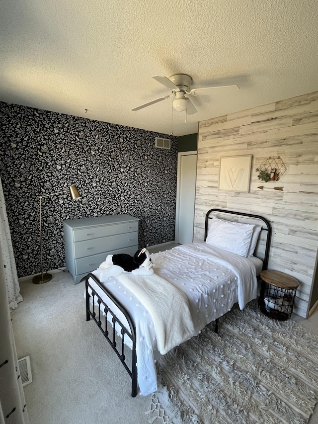 bedroom featuring carpet flooring, a ceiling fan, visible vents, wood walls, and a textured ceiling