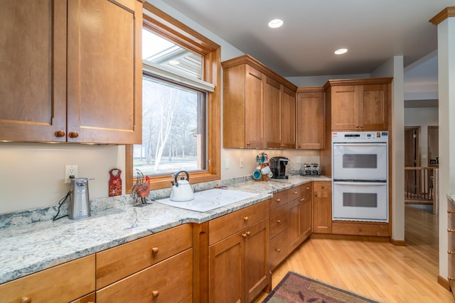 kitchen featuring white appliances, light stone countertops, brown cabinetry, and light wood-type flooring