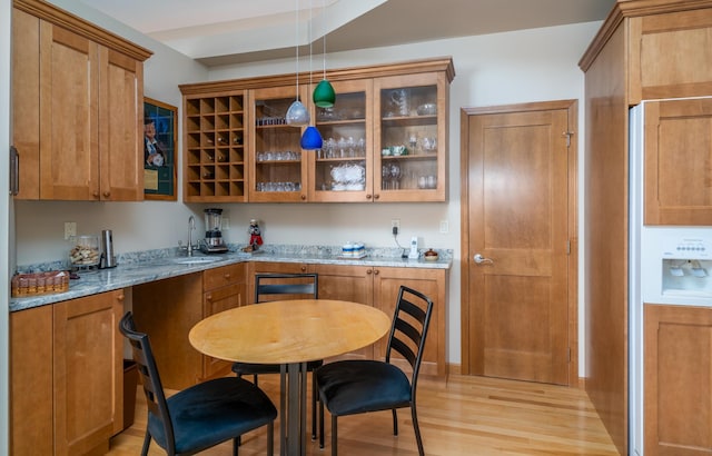 kitchen featuring light stone countertops, brown cabinets, light wood-type flooring, a sink, and glass insert cabinets
